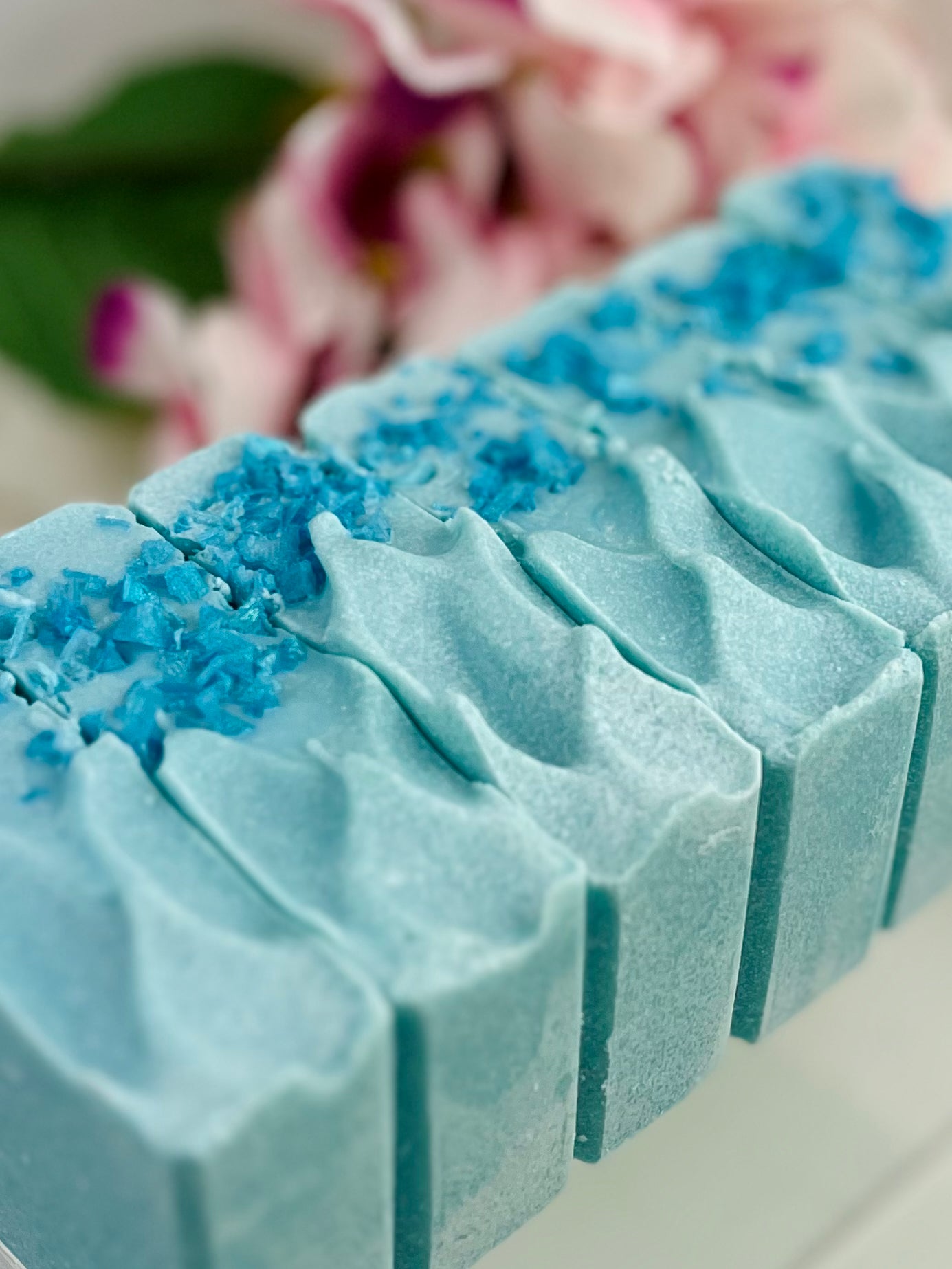Blue soap bar with decorative blue salt top on a blurred floral background