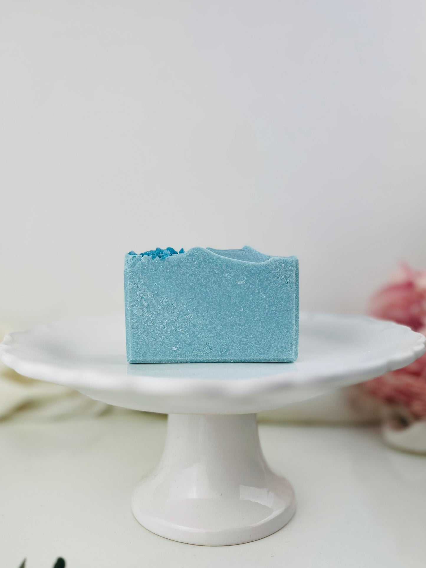 Blue salt soap bar on a white pedestal with a neutral background