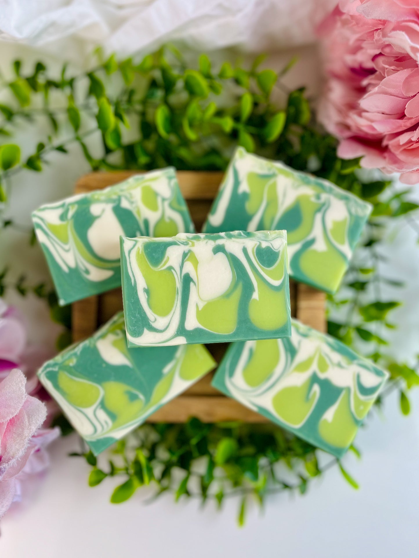 Green and white marbled soap bars on a wooden block with flowers in the background